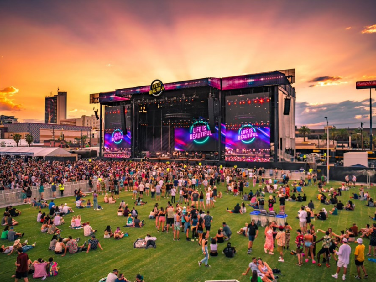 Large crowd on event turf at the "Life is Beautiful" festival in Las Vegas at night, with bright lights, a Ferris wheel, and the city skyline in the background.